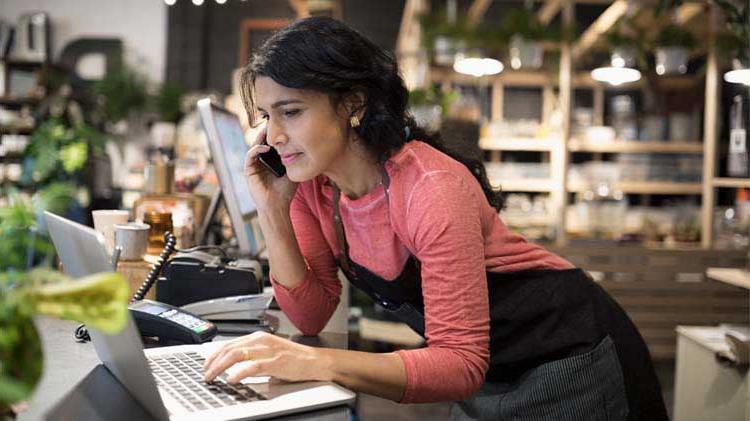 一名拥有一家小型创业公司的妇女正在她的花店用手机在笔记本电脑上打字.