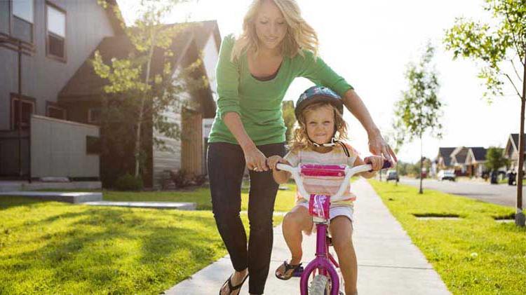Mom helping young daughter learn to ride her bike.